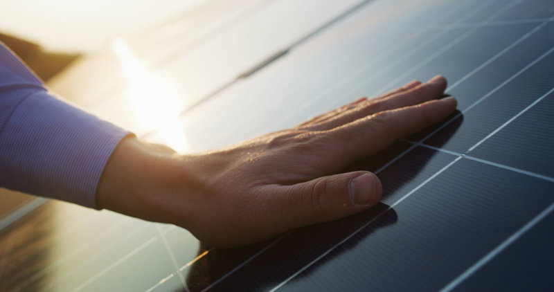 Nahaufnahme einer Hand eines jungen Ingenieurs ist die Überprüfung eines Betriebs von Sonne und Sauberkeit von Fotovoltaik-Solarpaneelen auf einem Sonnenuntergang. Konzept:erneuerbare Energien, Technologie, Strom, Dienstleistungen, umweltfreundliche Energie, Zukunft