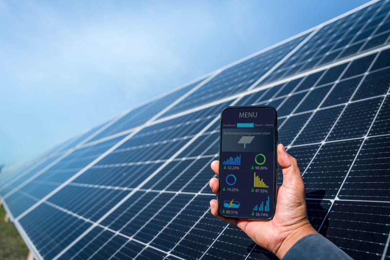 Mann Hand, die das Telefon für die Überwachung der Leistung in Solarkraftwerk (Solarzelle). Alternative Energie zur Energieeinsparung, Fotovoltaik-Modul-Idee für saubere Energieerzeugung.